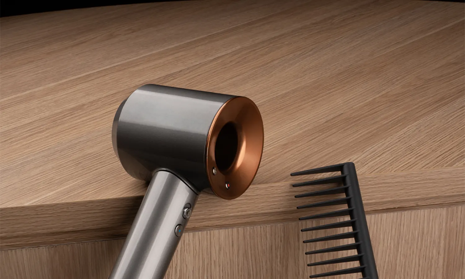 A Dyson hair dryer and comb on an oak surface